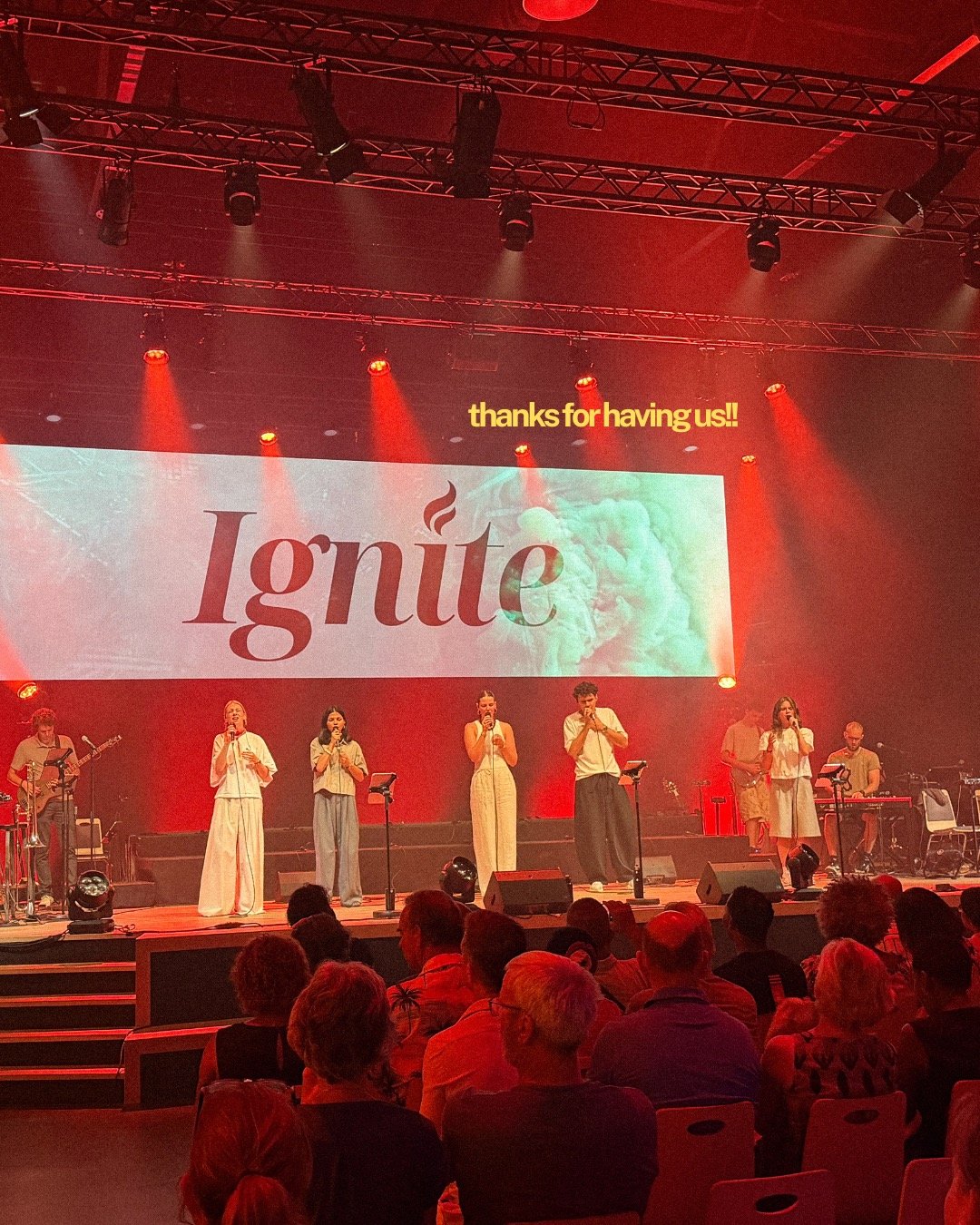 De band op een roodverlicht podium, het woord Ignite groot op het scherm